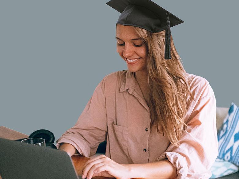 girl wearing mortarboard working on a computer